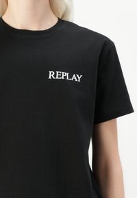 Black cotton t-shirt featuring white "REPLAY" text on the left chest area. It has a classic crew neckline and short sleeves.