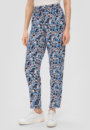 Pantaloni floreali con un motivo multicolore di blu, nero e rosa su uno sfondo chiaro; vita elastica, taglio dritto, indossati con sneakers bianche.