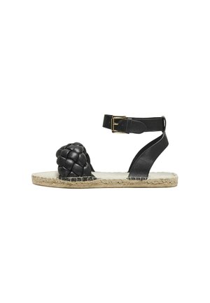Sandalia negra de cuero con tira trenzada, hebilla en el tobillo y suela de yute estilo espadrille. Presenta puntera redondeada y costuras en contraste.