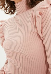 Maglione a coste di un delicato rosa chiaro con collo alto e dettagli arricciati sulle spalle. Presenta una forma aderente e una consistenza morbida.