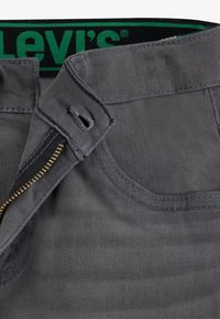 Grå denim jeans med metallglidelås og sømdetaljer. Har en svart linning med "Levi's"-logo i grønt.