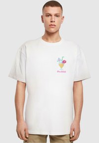 Hvid bomulds t-shirt med farverig broderi af en cocktail med parasoller og blomster. Korte ærmer og afslappet pasform.