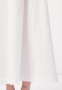Jupe longue blanche en tissu texturé avec de subtiles rayures verticales et un ourlet lisse, offrant une silhouette fluide et décontractée.