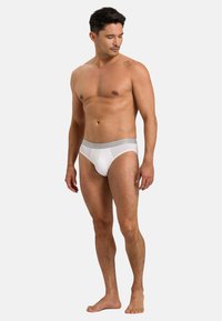 Slip bianchi da uomo realizzati in morbido tessuto, con un elastico grigio in vita che presenta il logo del marchio. Design aderente con copertura minima.