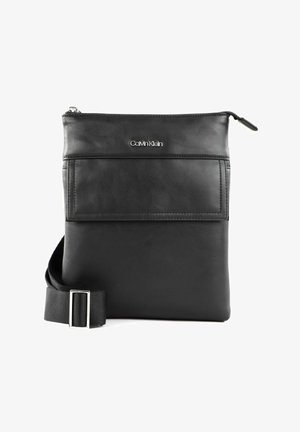 Sac bandoulière en cuir noir avec fermeture éclair, poche avant et sangle en satin réglable. Présente un logo embossé sur le devant.