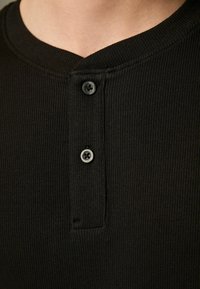 Sort ribbet bomulds henley skjorte med en rund krave og tre sorte knapdetaljer på placket. Glat tekstur.