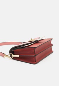 Červená kožená kabelka s růžovými akcenty, zlatými detaily, plochým obdélníkovým tvarem a strukturovaným tělem s kontrastním černým lemem.