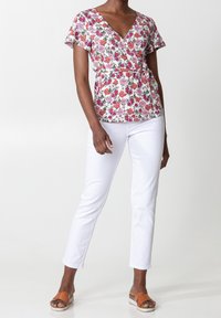 Blus med blommönster, V-ringning, korta fladdrande ärmar och markerad midja. Matchas med vita smala byxor och bruna platta sandaler.