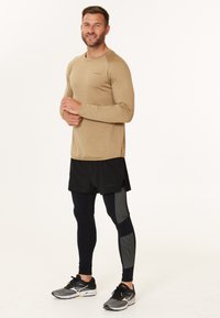 Langærmet, lysebrun træningsskjorte med tekstureret stof, parret med sorte shorts og tætsiddende marineblå leggings med grå detaljer.