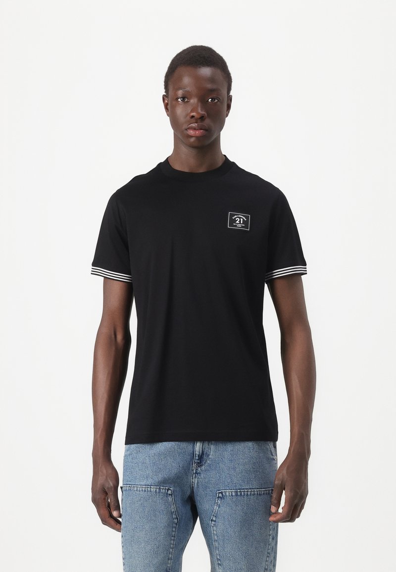 T-shirt preta de mangas curtas, com punhos listrados em branco, decote redondo e um pequeno rótulo frontal com detalhes em texto.