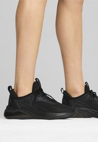 Zwarte sportieve schoenen met een bovenwerk van mesh, gestructureerde overlays, vetersluiting en een gevoerde zool voor ondersteuning en comfort.