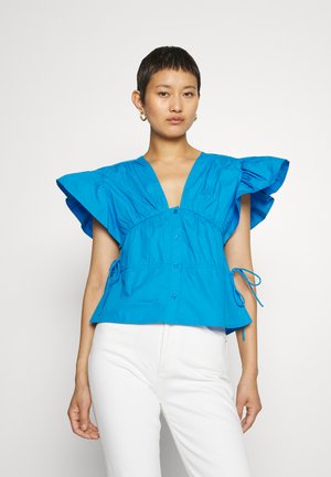 Φωτεινό μπλε πουκάμισο με φουσκωτά μανίκια, σφιχτή μέση και ρυθμιζόμενους σφιγκτήρες στα πλαϊνά; κατασκευασμένο από ελαφρύ ύφασμα.