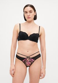 Zwarte kanten beha met beugels en verstelbare bandjes, gecombineerd met doorzichtige zwarte slips met roze bloemenborduursel en decoratieve bandjes.