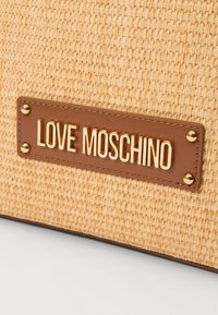 Woven beżowa torba o teksturowanej powierzchni, z brązową skórzaną metką wytłoczonym napisem "LOVE MOSCHINO" oraz złotymi akcentami.