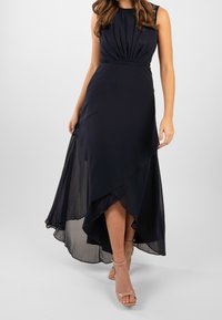 Abito maxi blu navy con corpino aderente, dettagli plissettati e orlo asimmetrico; realizzato in tessuto morbido con uno strato trasparente nella parte inferiore.