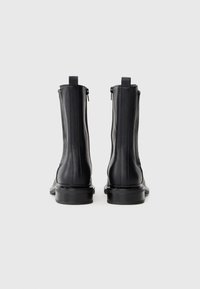 Black leather ankle boots with a smooth texture, featuring side zippers, a rounded toe, and a sturdy heel. Rear view shows minimal detailing.