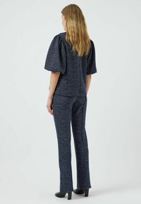 Completo due pezzi texturizzato blu navy composto da un top corto a maniche puff e pantaloni slim-fit, abbinato a scarpe nere con tacchi alti.