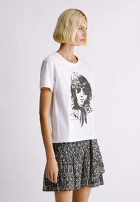 Witte katoen t-shirt met een zwart grafisch print van een gezicht, gecombineerd met een zwart-wit patroon skaterskirt.