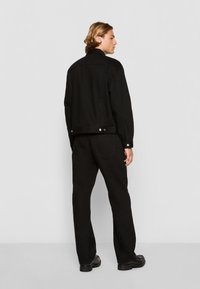 Black denim jacket with a collar, side pockets, and button closures, paired with matching black pants and sturdy black footwear.