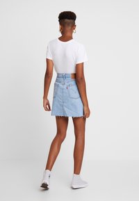 Světle modrá džínová minisukně s ošuntělým lemem, vysokým pasem a zadními kapsami. Kombinována s jednoduchým bílým tričkem a světle šedými teniskami.