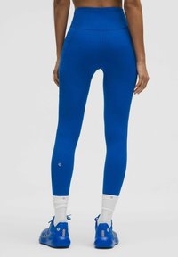 Aukštai įsegamos, prie kūno priglundančios kelnės solidžios mėlynos spalvos, pasižyminčios lygiu paviršiumi ir diskretišku šonu kišeniu. Pabrėžtos logotipo ir subtilių detalių akcentais.