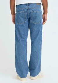 Vide bukser i lys blå denim med en falmet tekstur. Har to baklommer og en standard linning. Stylet med hvite joggesko.