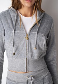 Gray cropped hoodie in soft fabric, featuring a gold zipper, front pockets, drawstrings, and ribbed hem. Paired with matching gray bottoms.