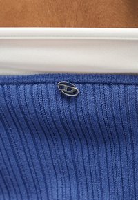 Κοντινό πλάνο της περιοχής γύρω από το ισχίο που δείχνει λευκό και μπλε ριγωτό ύφασμα με ένα μικρό ασημένιο οβάλ κούμπωμα προσαρτημένο στο μπλε ύφασμα.