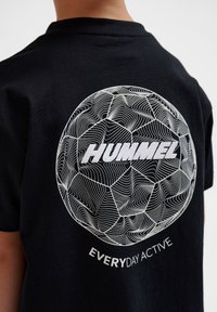Svart bomullströja med ett cirkulärt, vitt linjetecknat mönster som liknar en fotboll, med "HUMMEL" och "EVERYDAY ACTIVE" i fet stil.