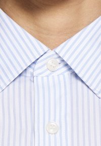 Colletto di camicia a righe azzurre e bianche con una pattina di bottoni dotata di bottoni in plastica bianchi. Tessuto liscio con un aspetto fresco.