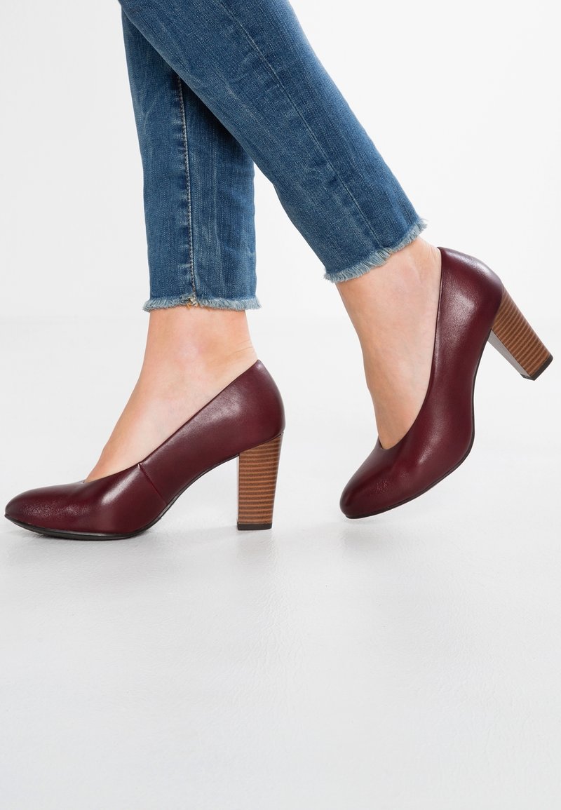 Chaussures à talons hauts en cuir bordeaux avec un bout rond et un talon en bois. Portées avec un jean en denim à ourlet effiloché.