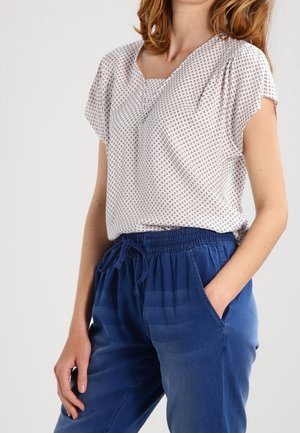 Blusa leggera a maniche corte di colore bianco con piccoli pois blu navy. Abbinata a pantaloni blu con cordoncino a vita alta, dal fitting rilassato, dotati di tasche laterali.