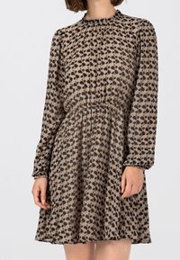 Hnědé šaty s vzorem, dlouhými rukávy, nařaseným výstřihem a elastickým pasem. Lehčí, průhledná tkanina s volným střihem.