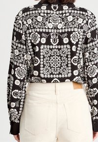 Chemise à motifs floraux noir et blanc avec manches longues, poignets à boutons et coupe ajustée, associée à un pantalon taille haute beige clair.