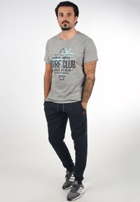 Gray cotton t-shirt with "Surf Club" graphic and palm tree design, paired with navy joggers and gray athletic shoes with white stripes.
