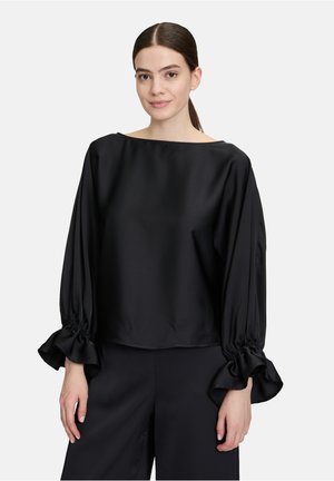 Blusa nera in satin con scollo a barca, maniche lunghe a sbuffo con polsini arricciati e vestibilità comoda. Texture liscia e design minimalista.