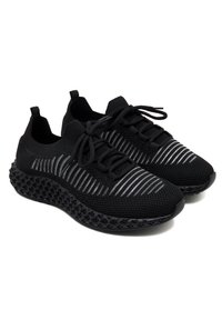Schwarze Sportschuhe mit einem gestrickten Obermaterial, das graue Streifenakzente aufweist. Die Sohle ist strukturiert und hat ein perforiertes Design für Grip und Flexibilität.