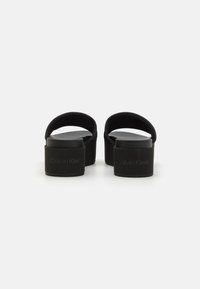 Sandales à plateformes noires avec une texture lisse, un dos ouvert et une forme arrondie. Présentent une semelle intérieure moulée et un logo de marque subtil au niveau du talon.