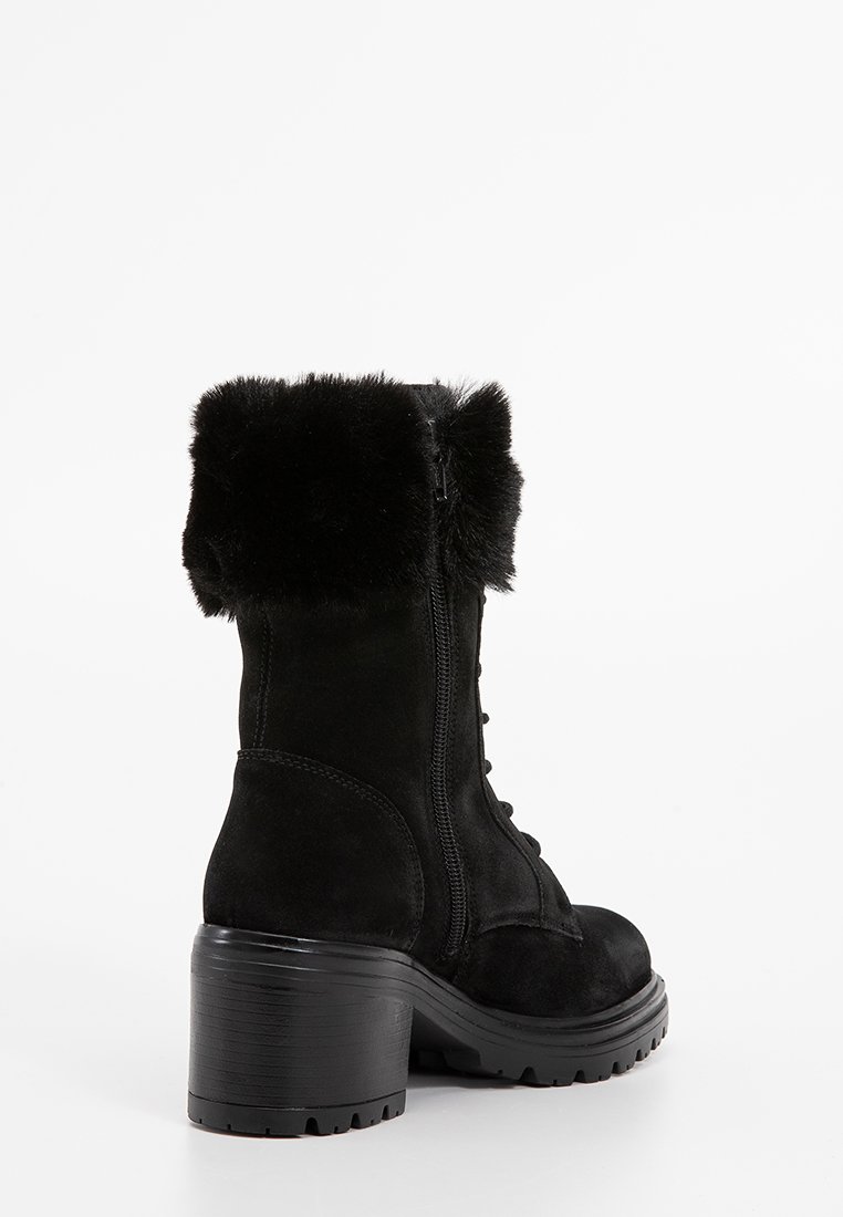 Botín de ante negro con un puño de pelaje sintético, cordones en la parte delantera y cremallera lateral. Presenta un tacón grueso y texturizado y una suela de goma para mayor agarre.
