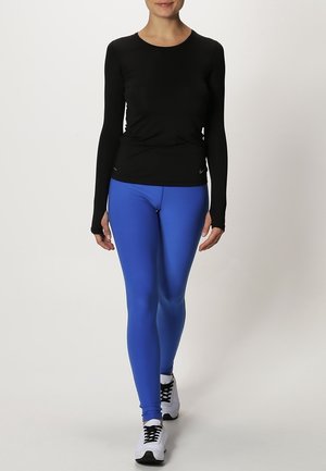 Černý dlouhý rukáv sportovní top v kombinaci s modrými legínami, vyrobený z elastického materiálu, s přiléhavým střihem a bílými teniskami.