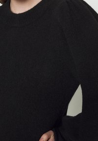 Svart tröja gjord av mjukt, strukturerat material. Har en rundad halsringning och puffärmar. Närbild av tyget och detaljer.