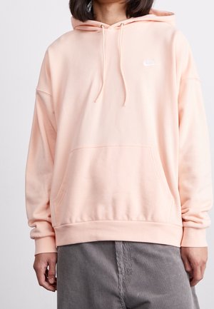 Sudadera rosa clara con un corte holgado, cordones, bolsillo frontal y un pequeño logo blanco de Nike en el pecho, fabricada en suave material de algodón.