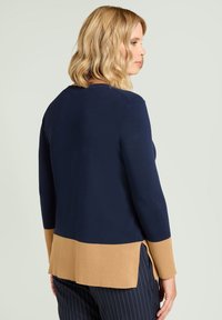 Suéter azul marino con detalles marrones en el dobladillo y las mangas, con una textura acanalada. Las aberturas laterales ofrecen mayor movilidad y comodidad.