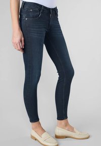 Jean skinny bleu foncé en denim, avec un design classique à cinq poches et de subtils détails de couture, associés à des mocassins beiges.