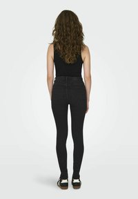 Jeans negros de cintura alta con una silueta ajustada, que cuentan con bolsillos traseros y una textura suave. Combinados con zapatillas negras.
