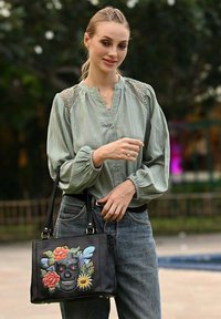 Zwarte leren handtas met bloemen- en doodskopborduursel. Heeft een gestructureerde vorm, dubbele handvatten en hardware-accenten. Getextureerde stof.