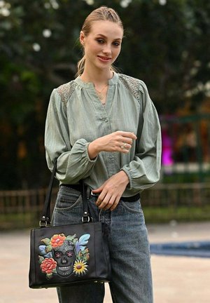 Zwarte leren handtas met bloemen- en doodskopborduursel. Heeft een gestructureerde vorm, dubbele handvatten en hardware-accenten. Getextureerde stof.
