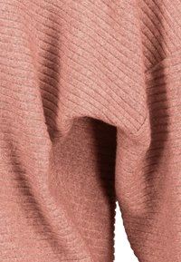 Nahaufnahme von weichem, geripptem Strickstoff mit gefaltetem Muster in Staubroséfarbe.