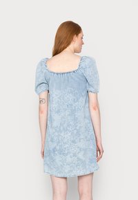 Vestido de ganga azul claro com mangas bufantes e decote quadrado, apresentando um padrão floral, detalhes franzidos ao longo do decote e um corte descontraído.