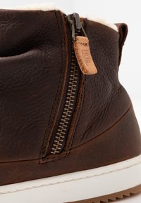 Brown leather boot featuring a side zipper, cream lining at the top, and a white rubber sole with a textured finish.